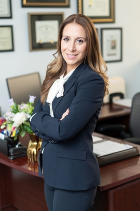 Attorney, Michele Ross, standing in front of her office desk, smiling, with her arms folded. 